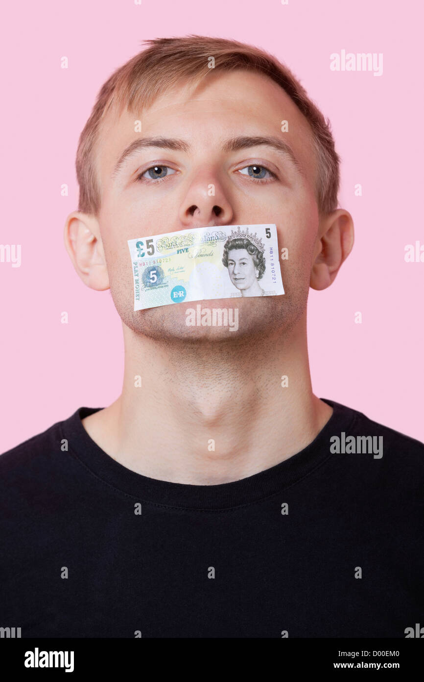 Portrait of a young man with paper money stuck over his mouth against pink background Stock Photo