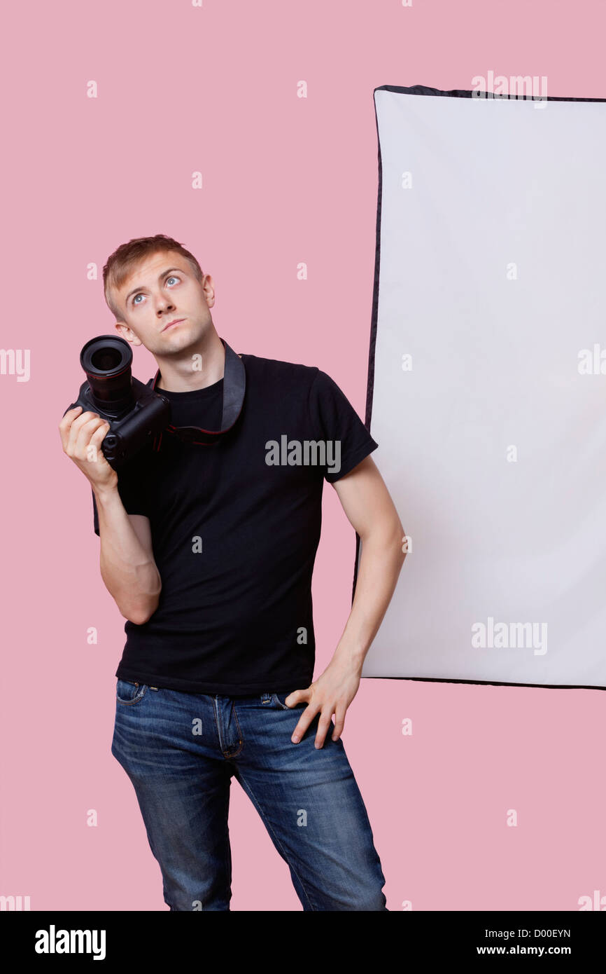 Bored young male photographer holding camera over pink background Stock Photo
