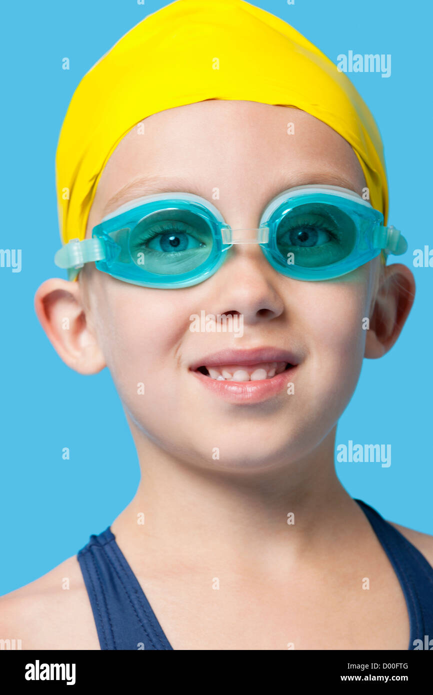 Close-up portrait of a happy young girl wearing swim cap and goggles over blue background Stock Photo