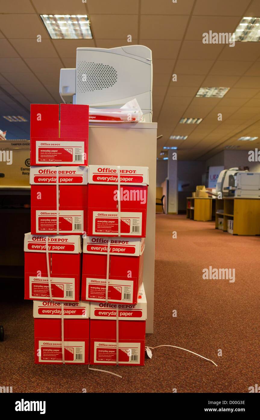 A pile of boxes containg reams of printer paper on the floor of an open plan office. Stock Photo