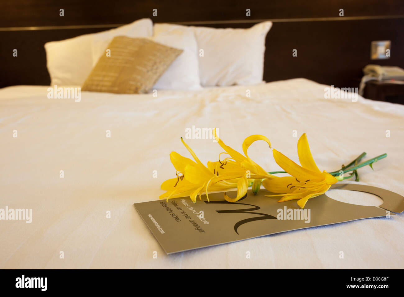 Flowers and Do Not Disturb sign lying on a hotel bed. Stock Photo