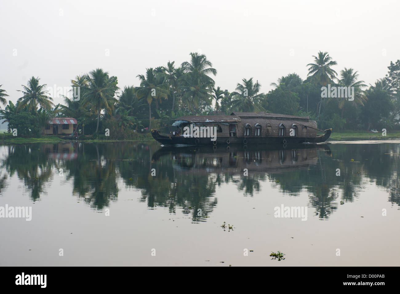 Tourist rice barge passing reflections on the West Coast Canal (National Waterway No 3) at sunrise, Kanjippadom, near Alappuzha (Alleppey), Kerala, India Stock Photo