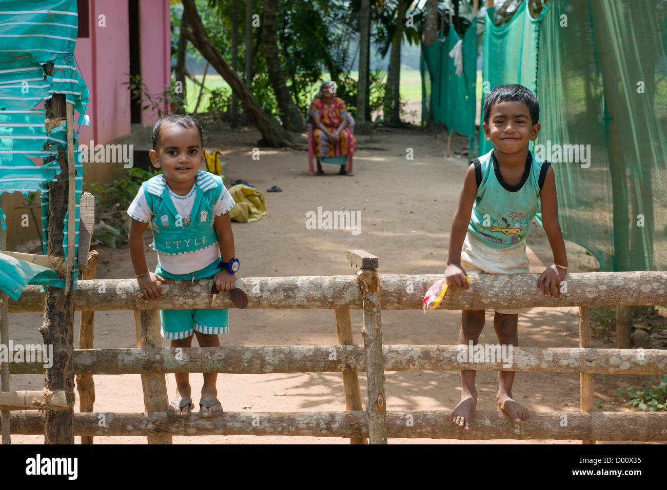 Two boys climbing on a fence with their mother sitting behind, Kanjippadom, near Alappuzha (Alleppey), Kerala, India Stock Photo
