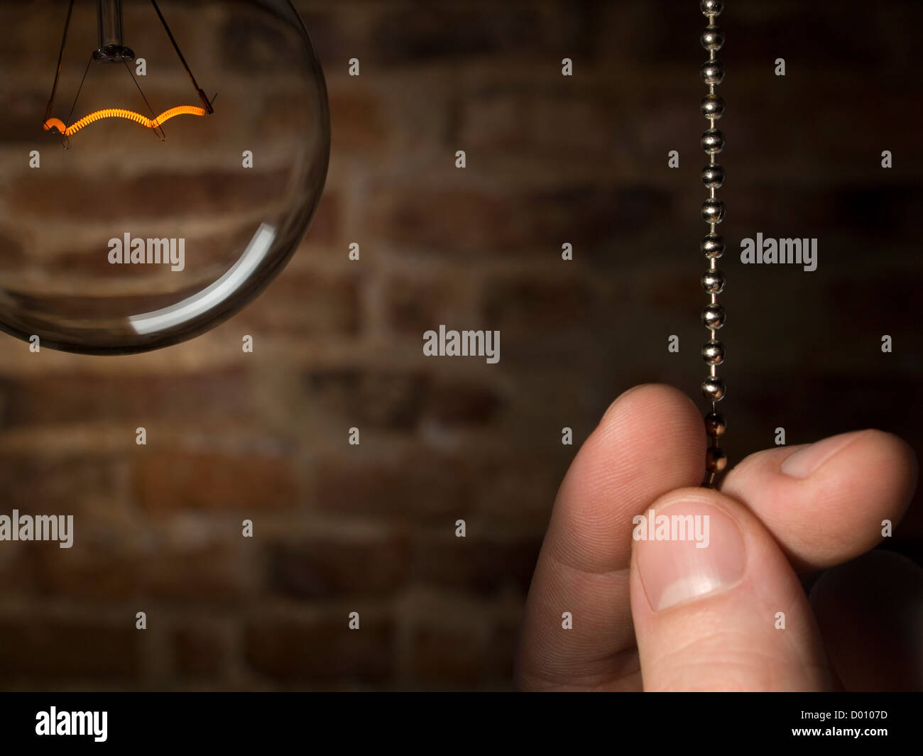 A man's hand is about to switch off the bulb light. Brick wall as background. Stock Photo