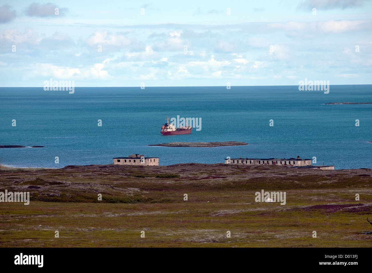 Russian coast of Barents Sea with abandoned houses and big red ship Stock Photo