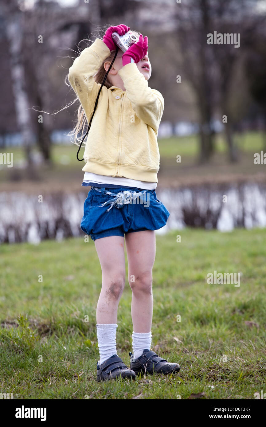 little funny girl bright color dressed with photo camera in the hands on neutral outdoor nature background Stock Photo