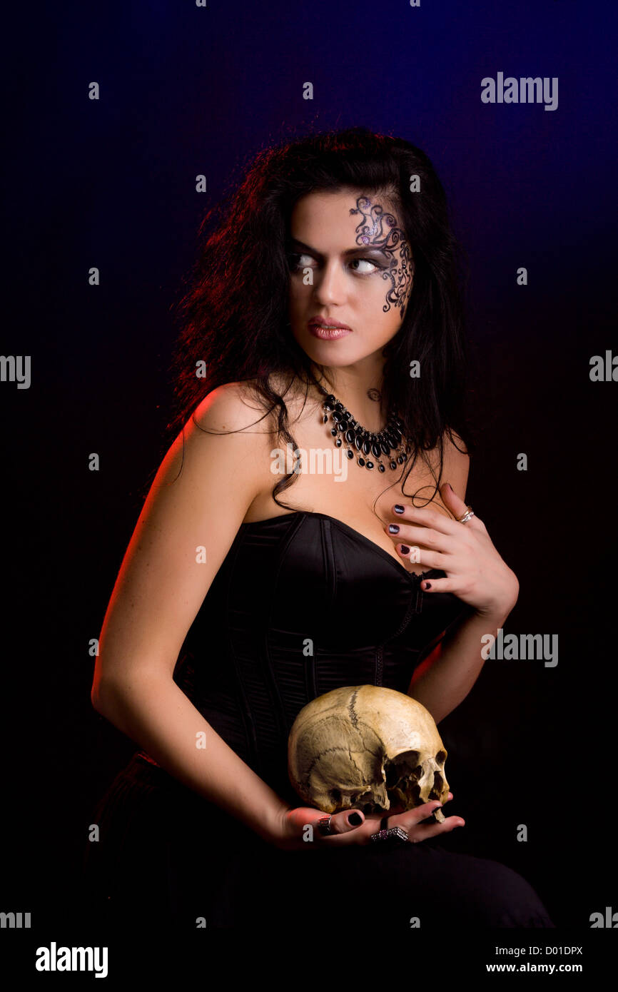 Young beautiful demonic female creature holding scull Stock Photo