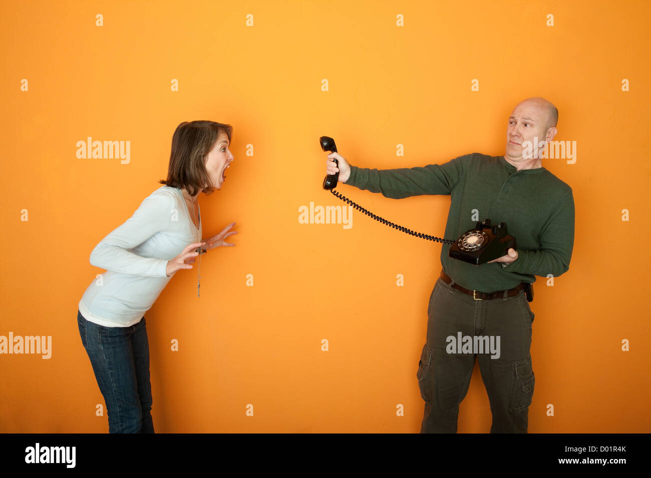 Man holds telephone while woman yells at it Stock Photo