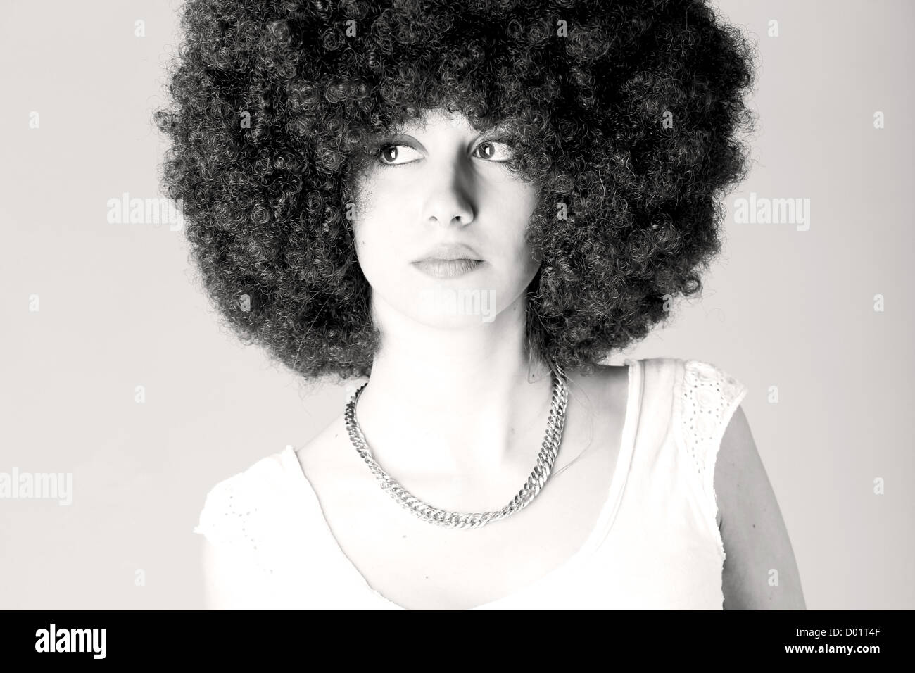 Young woman wearing an afro wig against gray background Stock Photo