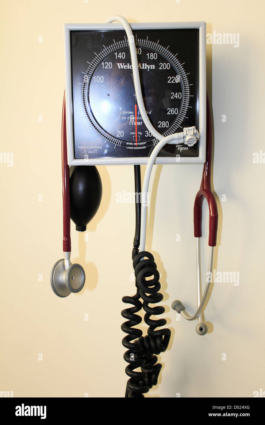 a blood pressure instrument gauge monitor on a wall in a hospital with a stethoscope hanging from it Stock Photo