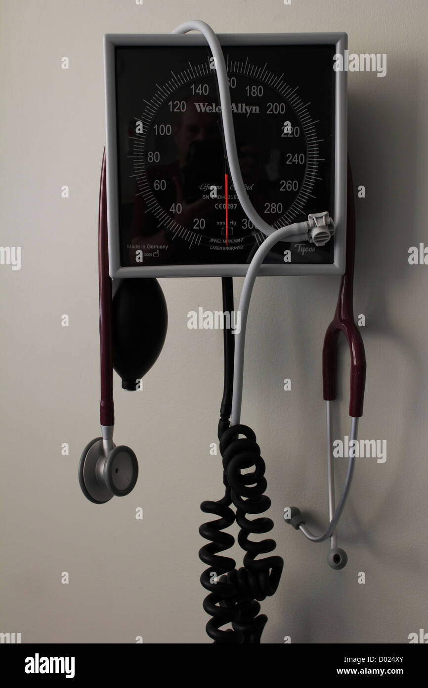 a blood pressure instrument gauge monitor on a wall in a hospital with a stethoscope hanging from it Stock Photo