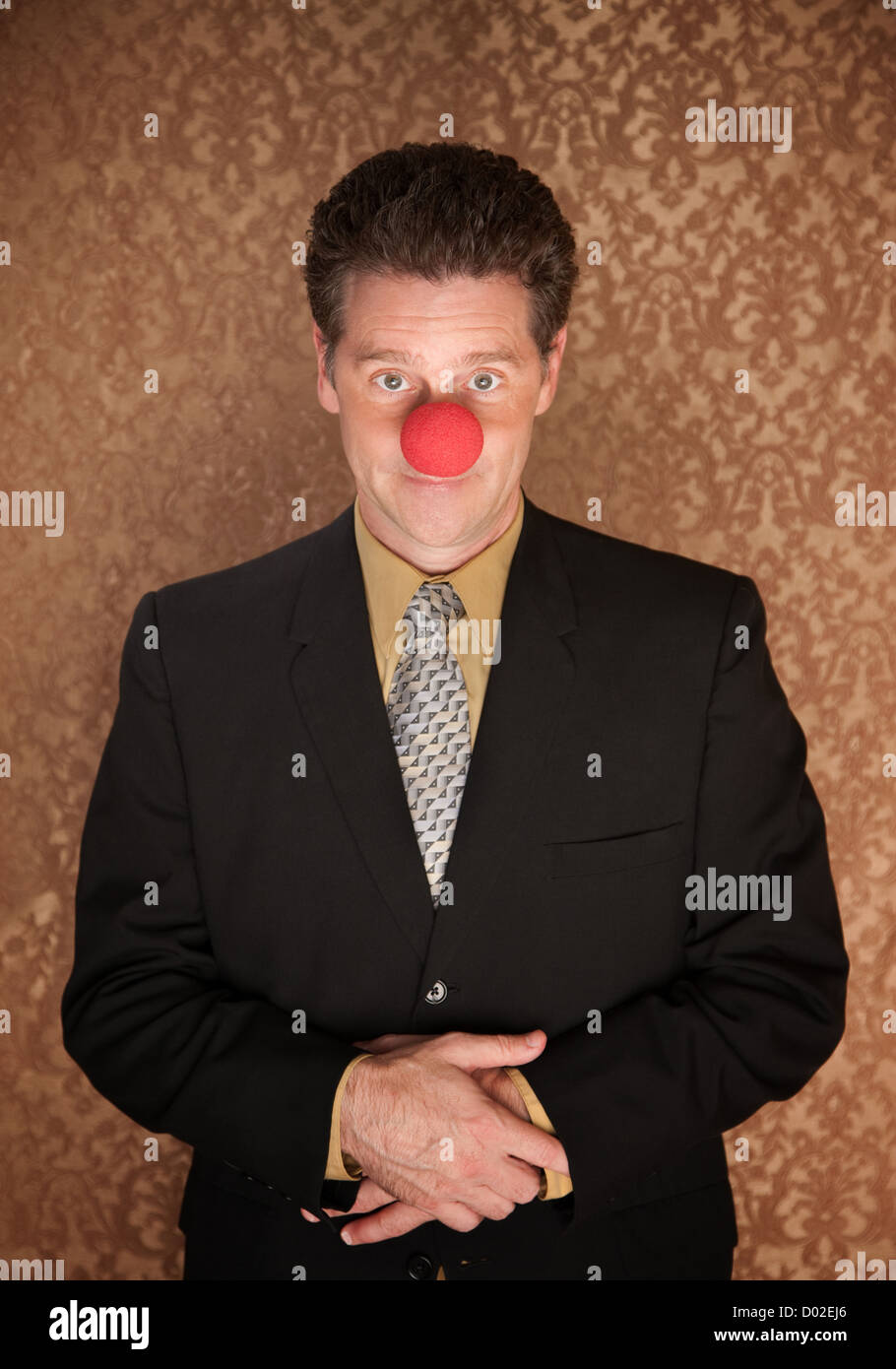 Young businessman with folded clasped hands and clown nose Stock Photo