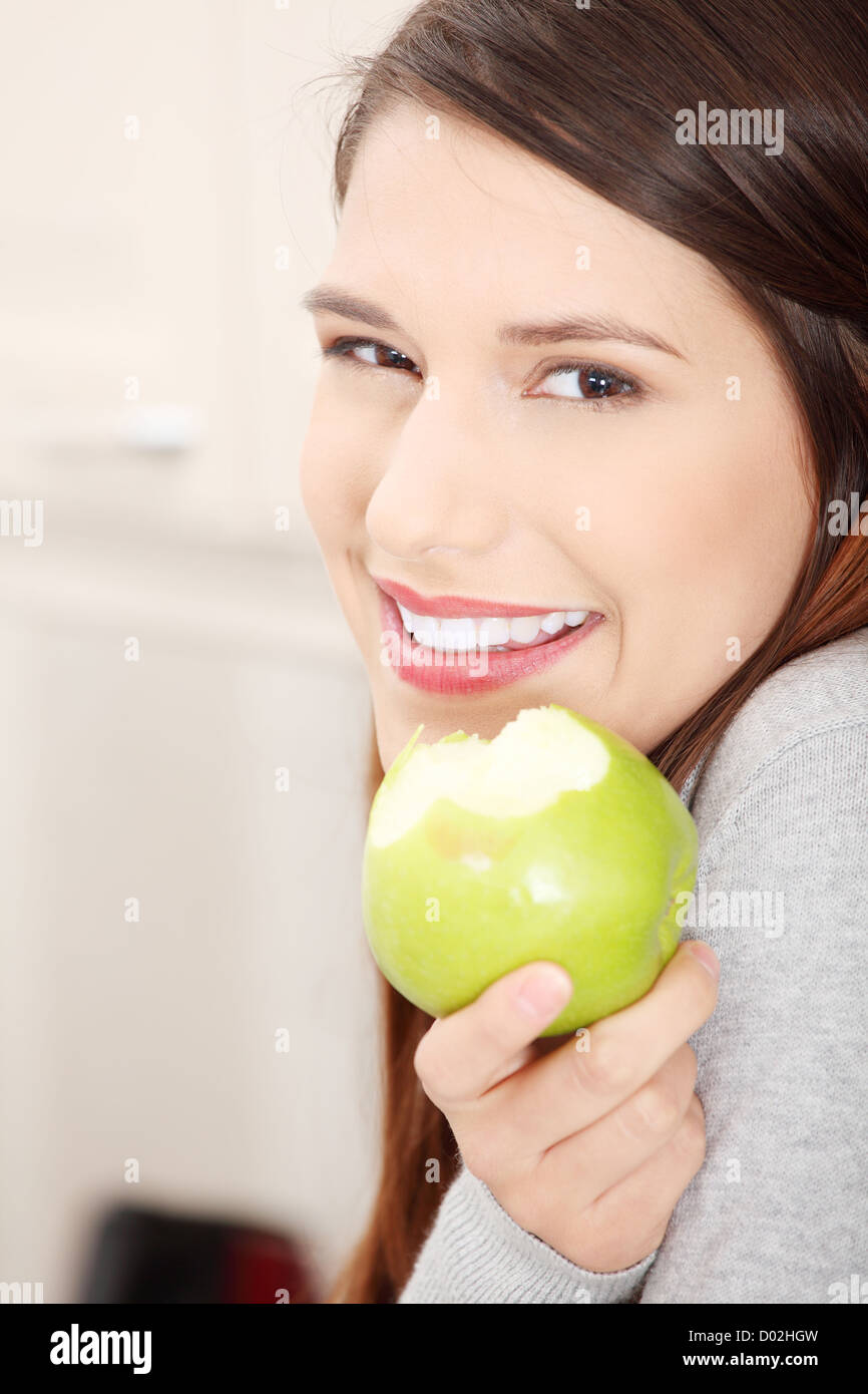 Young , happy, beautiful woman in kitchen eating green apple Stock