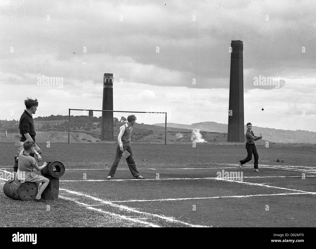 Boys playing tennis on home made court in Blowers Green Dudley with chimney stacks of Stourbridge Glazed Brick Company. Britain 1950s working class West Midlands children teenagers industrial heritage industry Stock Photo