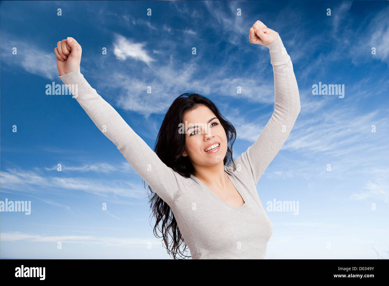 Happy young woman with arms up against blue sky Stock Photo - Alamy