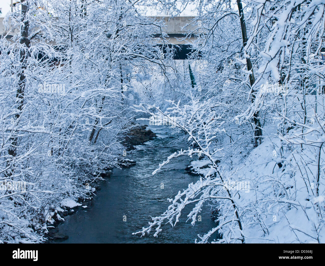 Blue and frosty, snowy winter scene with snow covered trees open river and concrete bridge in Oslo Norway Stock Photo