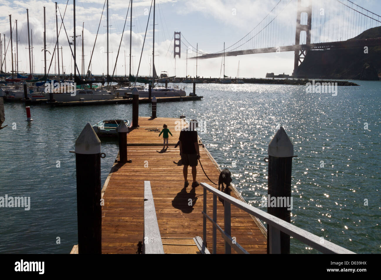 Man and boy walking dog on dock with the Golden Gate Bridge in San Francisco, California in the background. Stock Photo