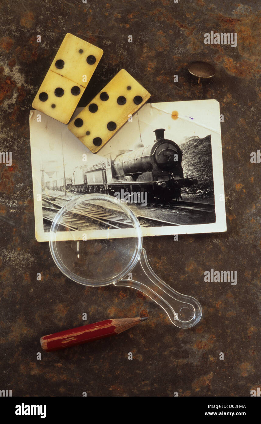 Black and white photo of steam loco on rusty metal sheet with dominoes magnifying glass pencil stub and drawing pin Stock Photo