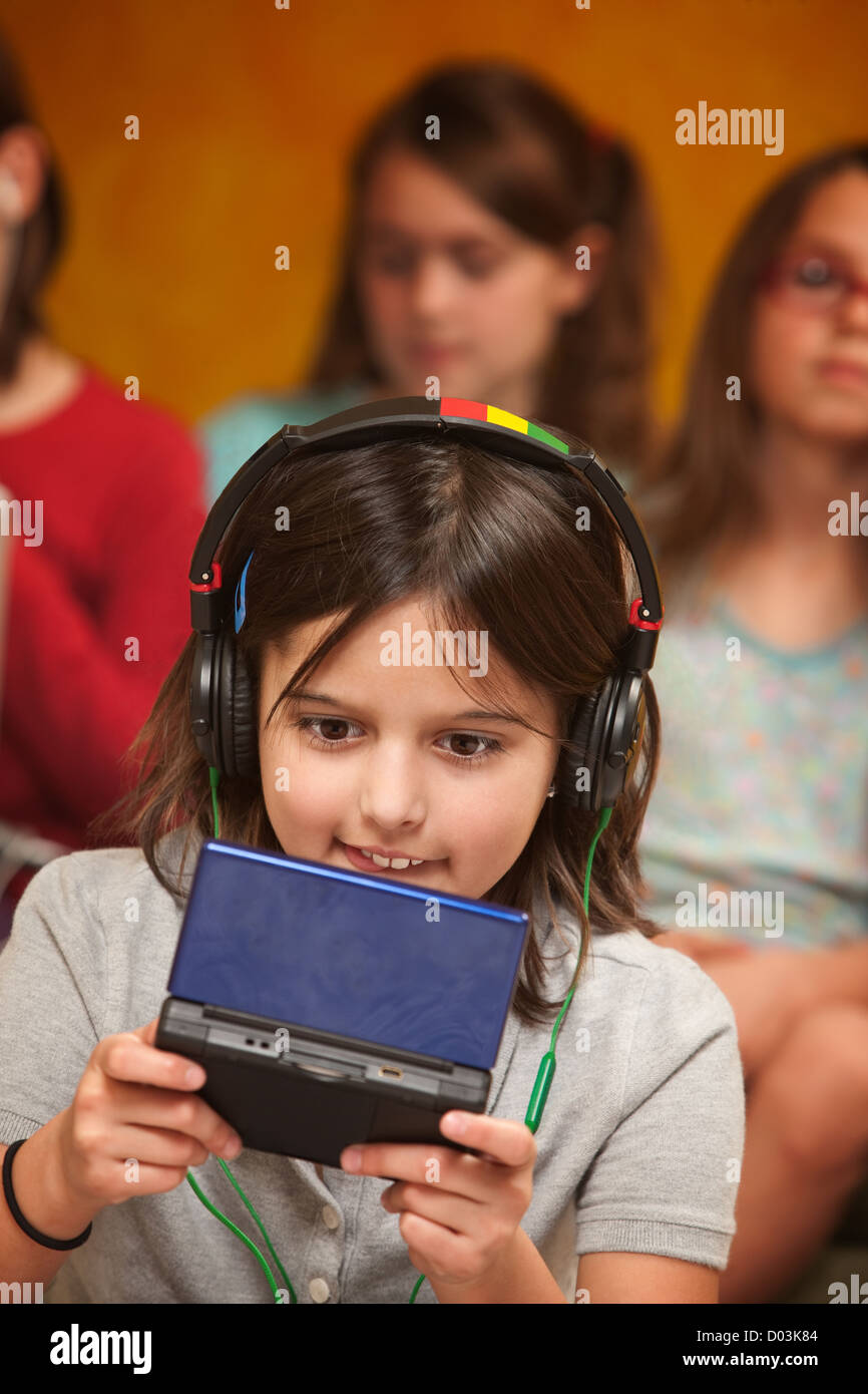 Little Caucasian girl with earphones plays a handheld video game Stock Photo