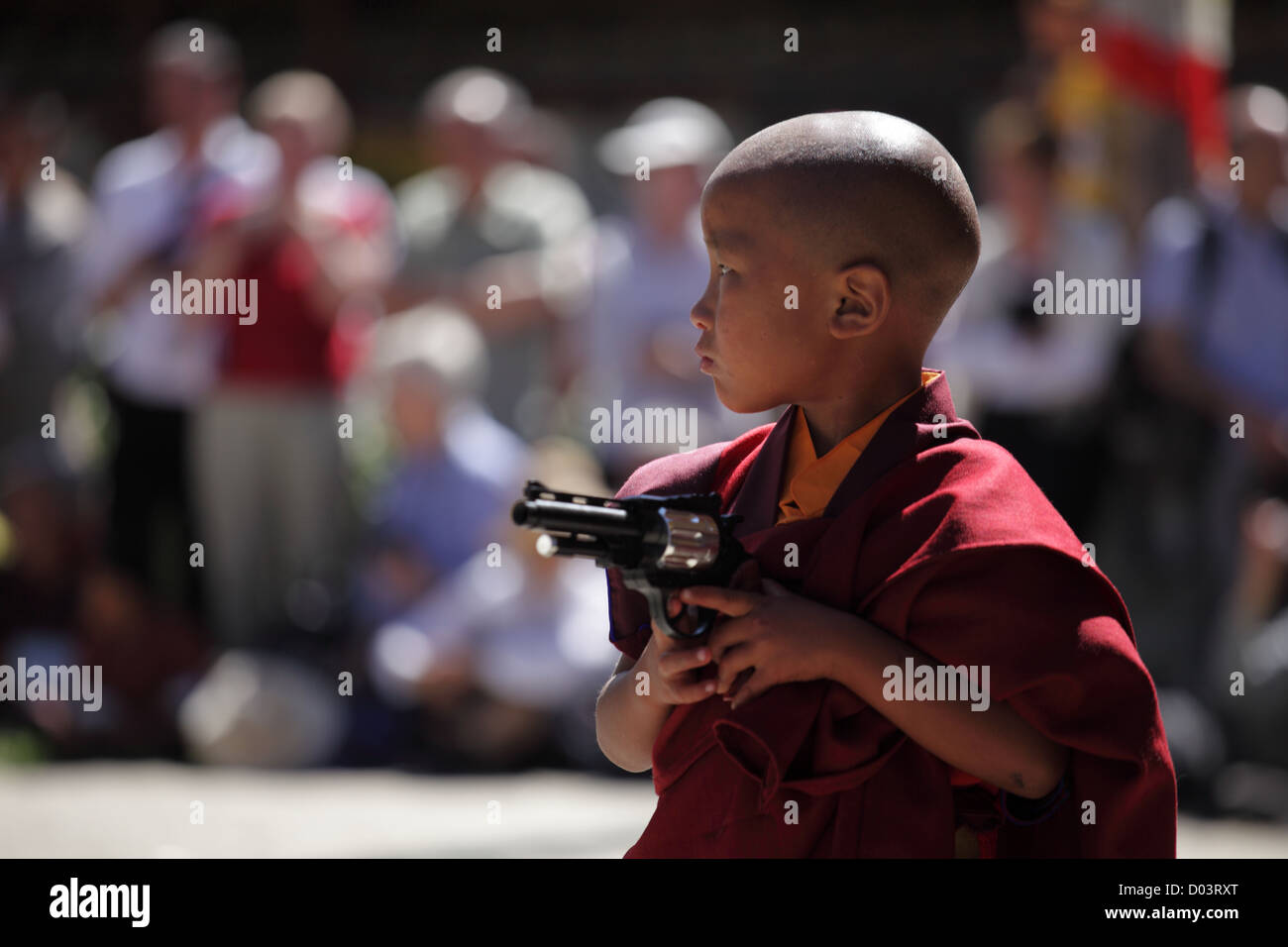 Little monk standing with a toy gun performing art at a festival in Bhutan Stock Photo