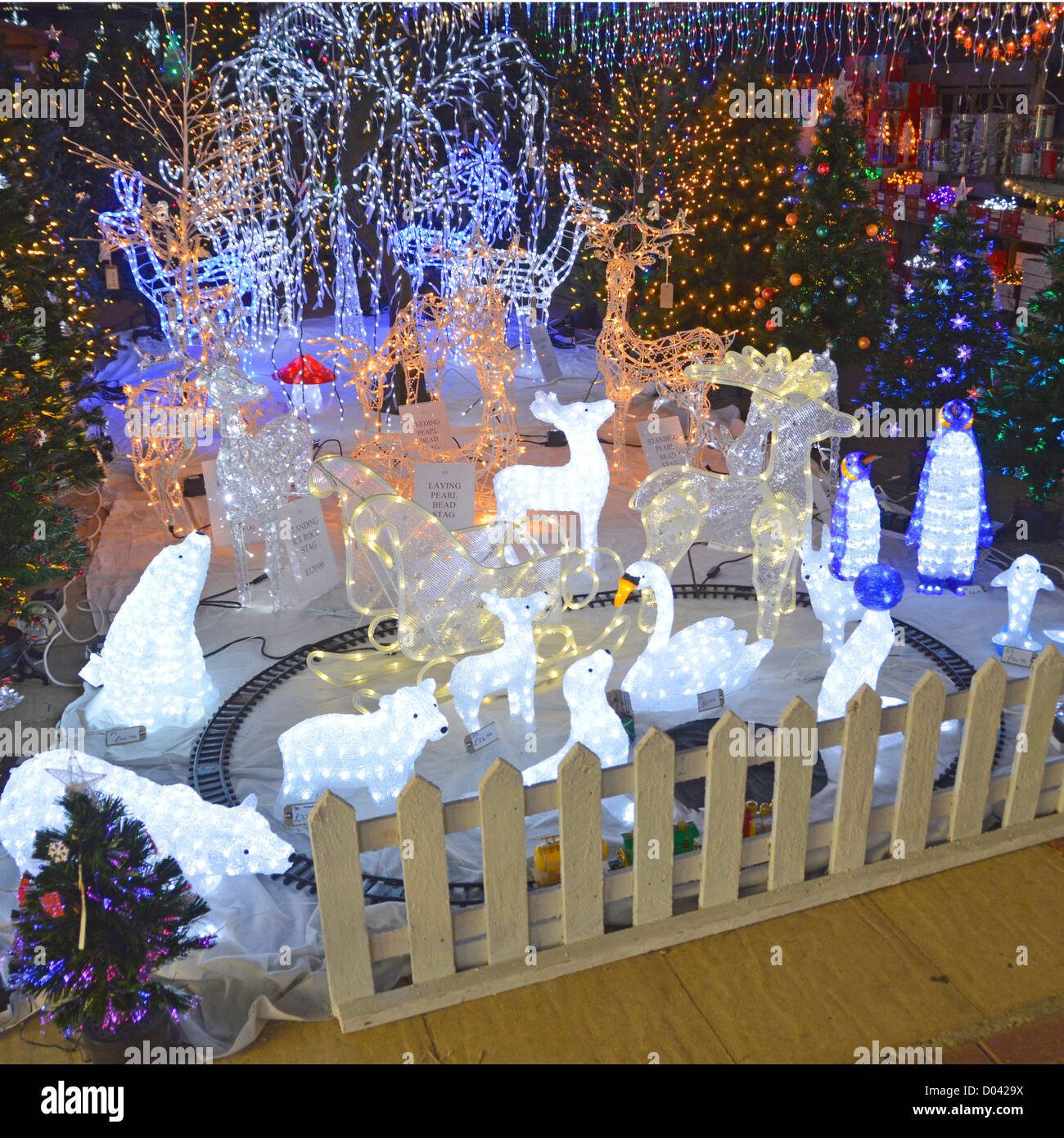 Display of illuminated Christmas trees & decorations on sale in a garden centre store Essex England UK Stock Photo