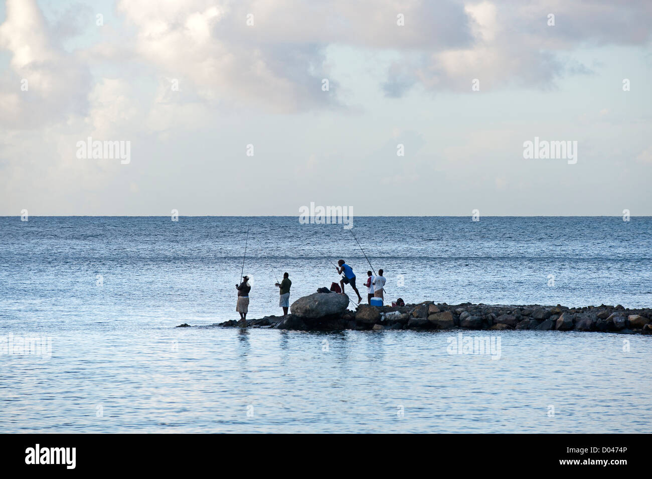 Fishermen stand with rods on promontory in St Lucia with view of horizon to sea. Stock Photo