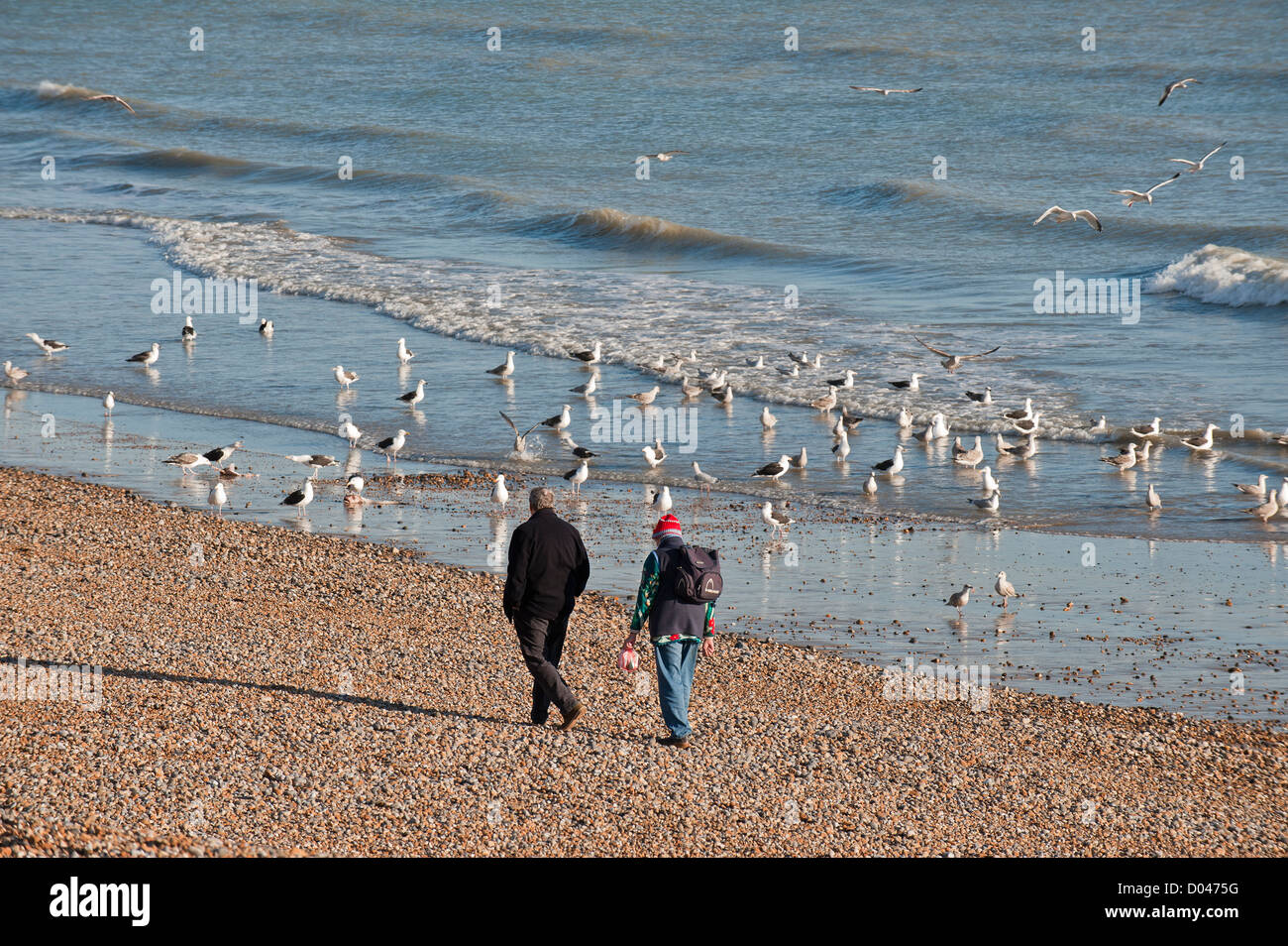 Two people walking along a beach in Hastings Stock Photo - Alamy