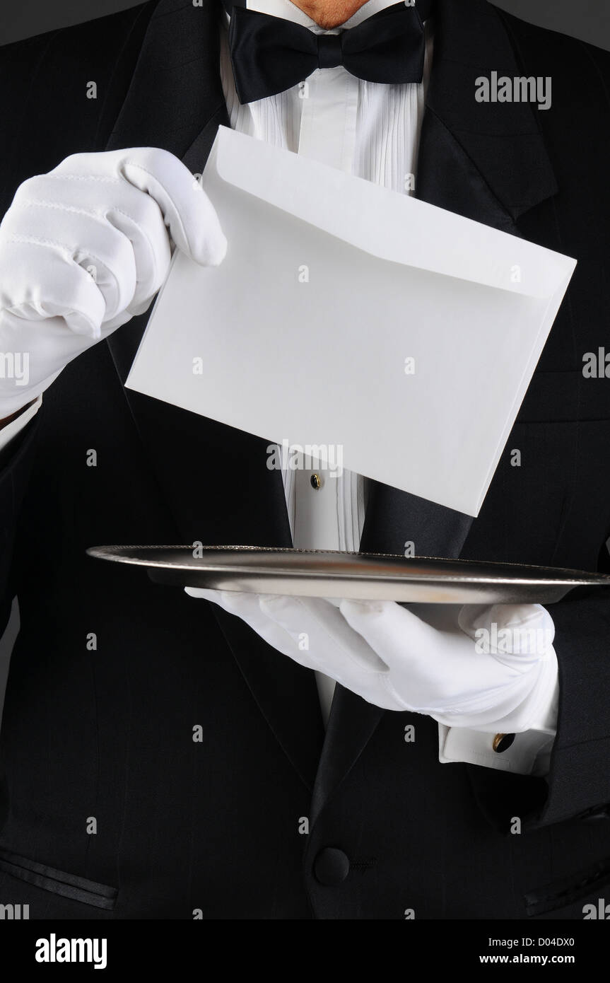 Closeup of a butler wearing a tuxedo holding a silver tray and an envelope. Vertical format, man is unrecognizable. Stock Photo