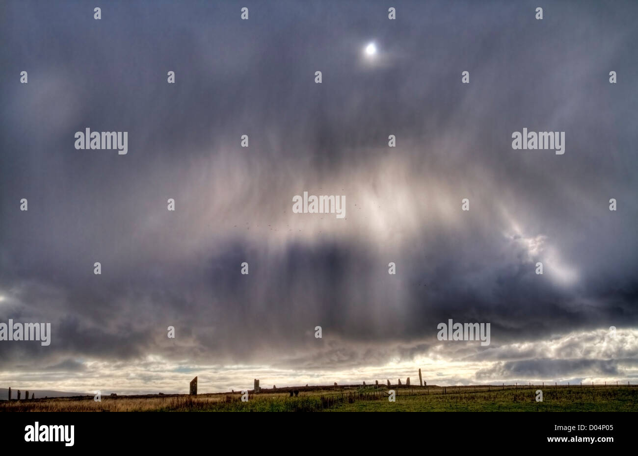A flock of birds fly through a bright patch in an atmospheric rainstorm over the Ring of Brodgar, Orkney. Stock Photo