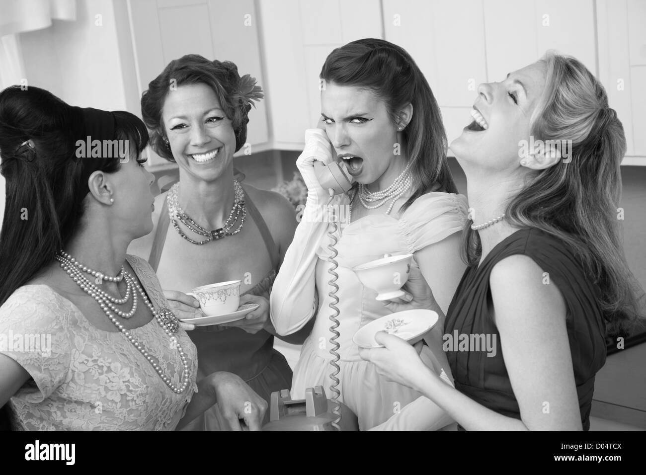 Outraged woman on phone with three friends in a kitchen Stock Photo