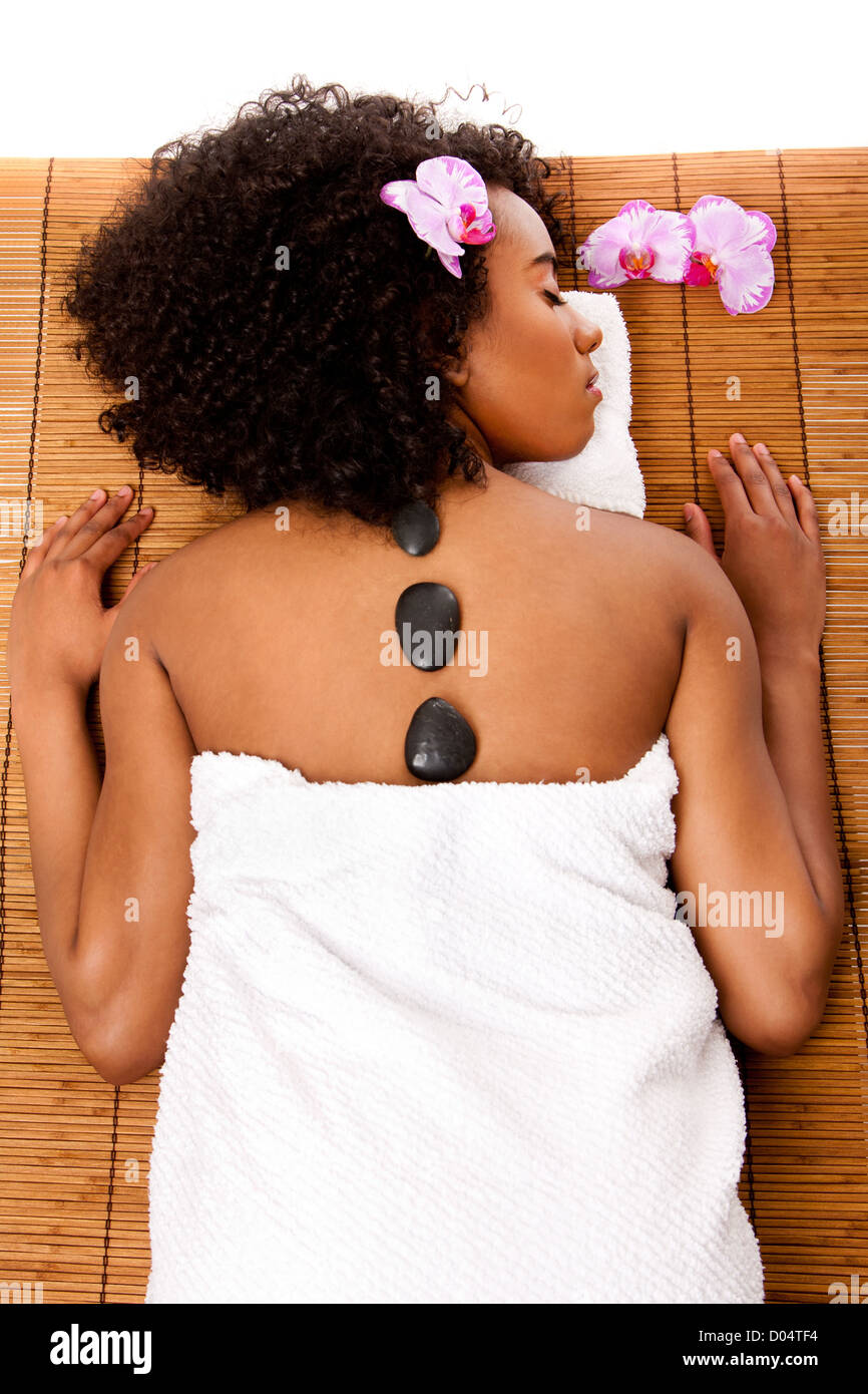 Latina-African woman health day spa hot lastone therapy massage laying in white towel on bamboo table decorated with orchids Stock Photo