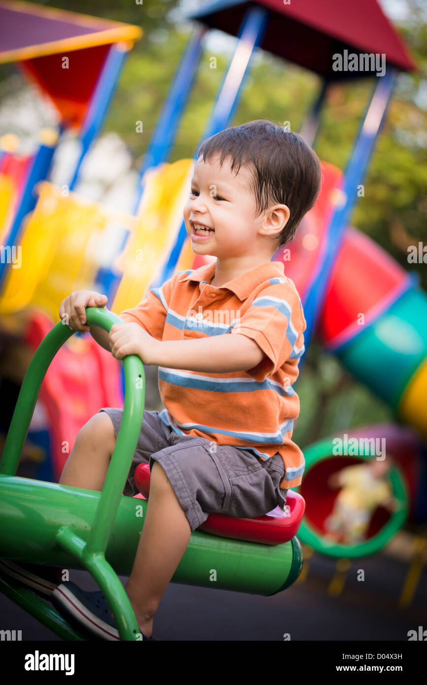Cheerful 2 year old boy riding a seesaw in an outdoor playground Stock
