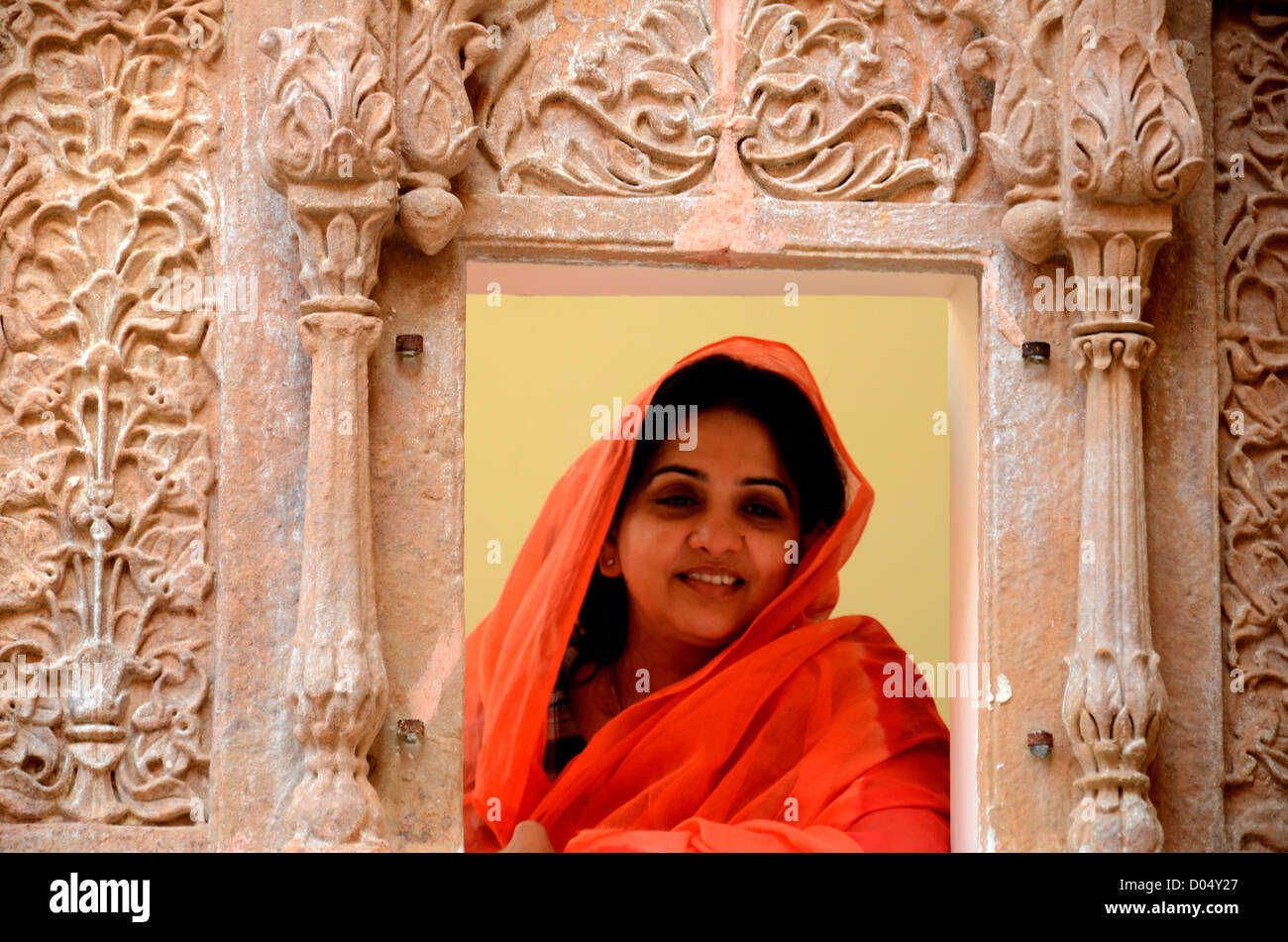 A woman in red duppatta looking through jharokha ( window) of a palace in Rajasthan,India Stock Photo