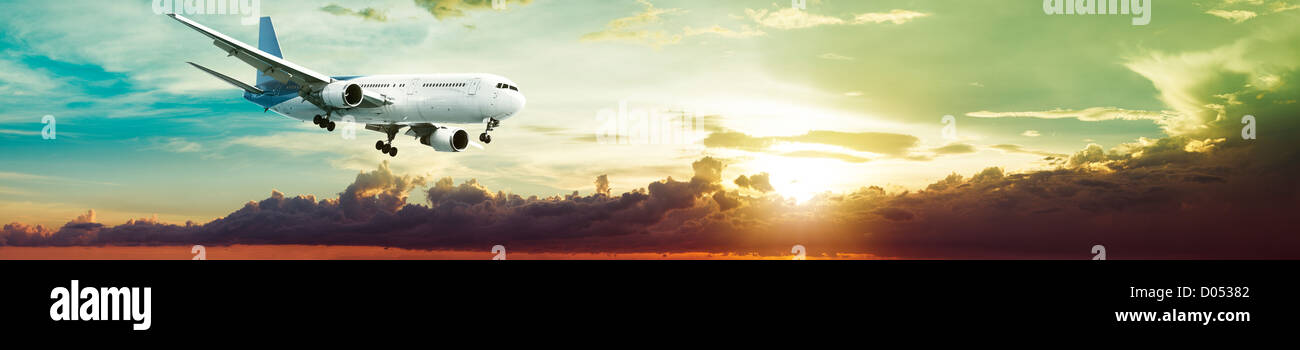 Jet plane is maneuvering for landing in a spectacular sunset sky. Panoramic composition. Stock Photo