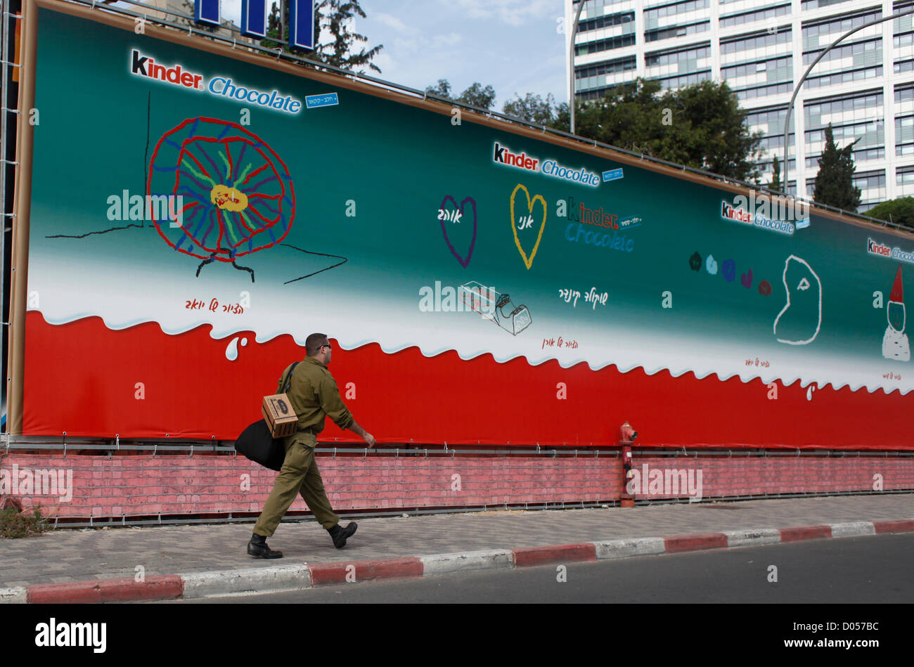 An Israeli reservist soldier carrying a gas mask box walks past an advertisement billboard advertising Kinder Chocolate in downtown Tel Aviv Israel Stock Photo
