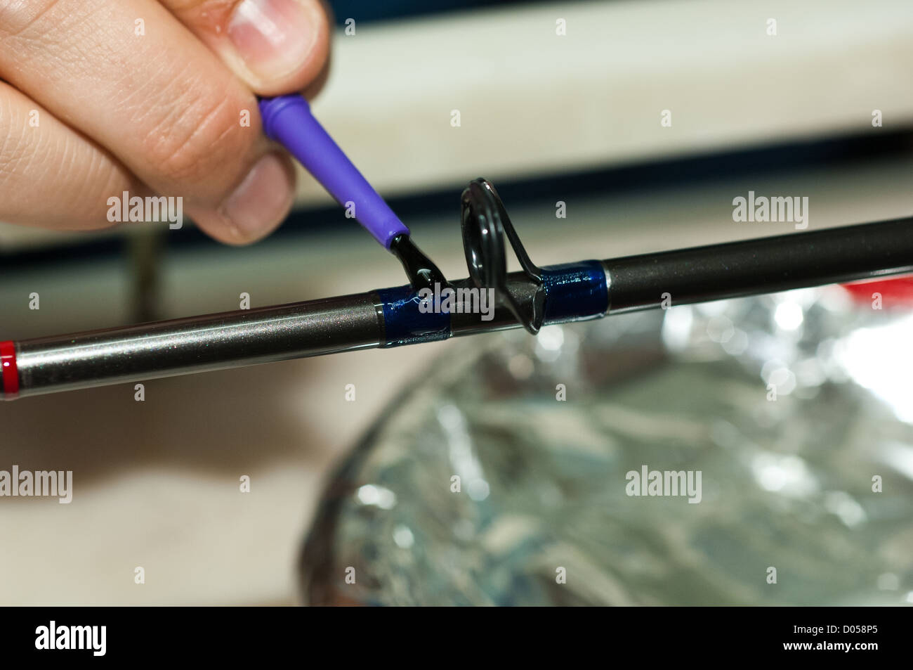 Fishing rod builder painting epoxy glue over thread wraps to secure the rod  guide Stock Photo - Alamy