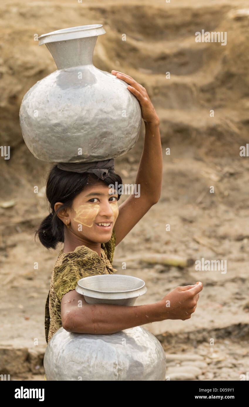 A girl carrying water up a steep riverbank in Pannmyaung using a water carrier typical of the type used in the region. Stock Photo