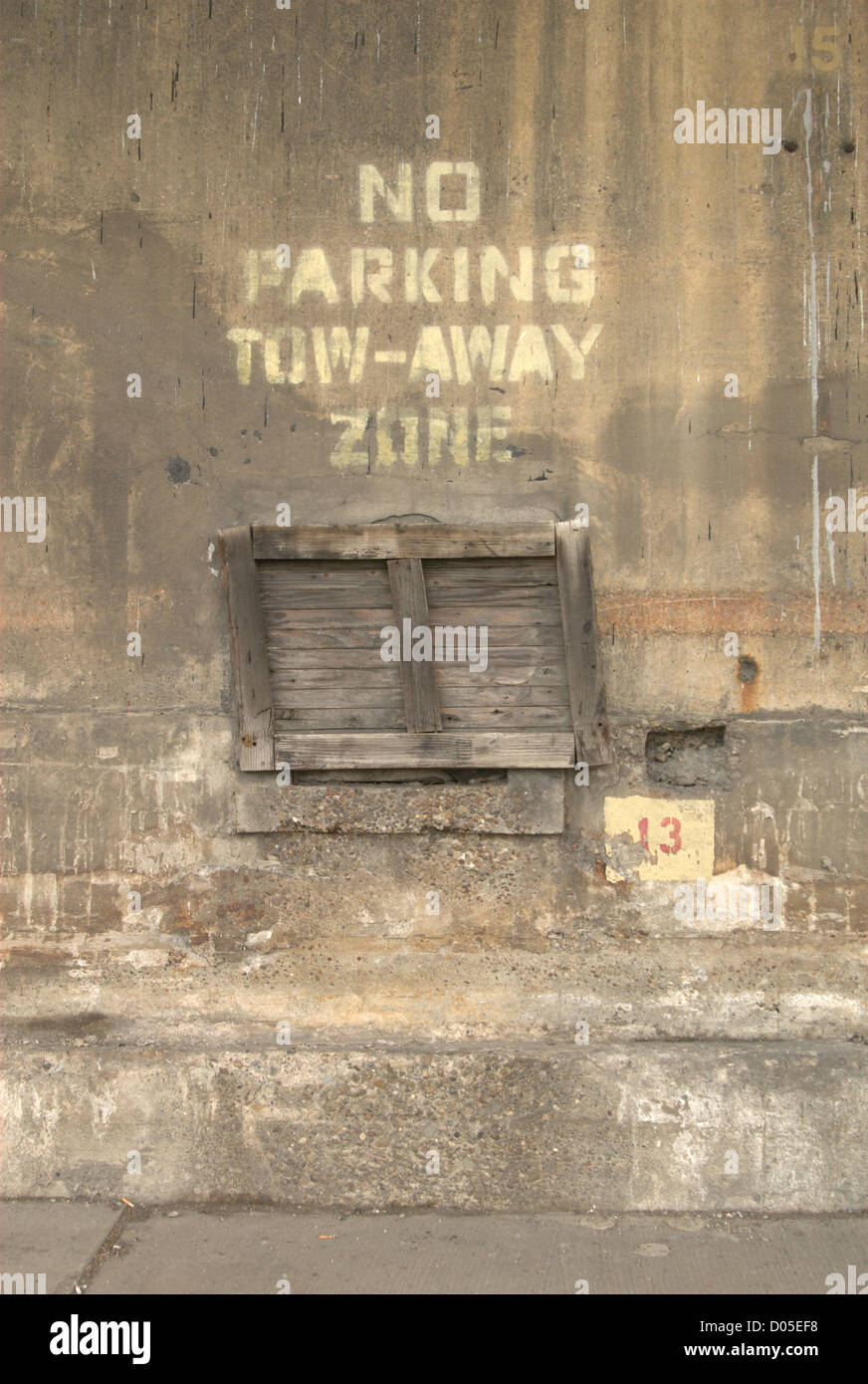 no parking tow away zone painted on concrete wall above boarded up window Stock Photo