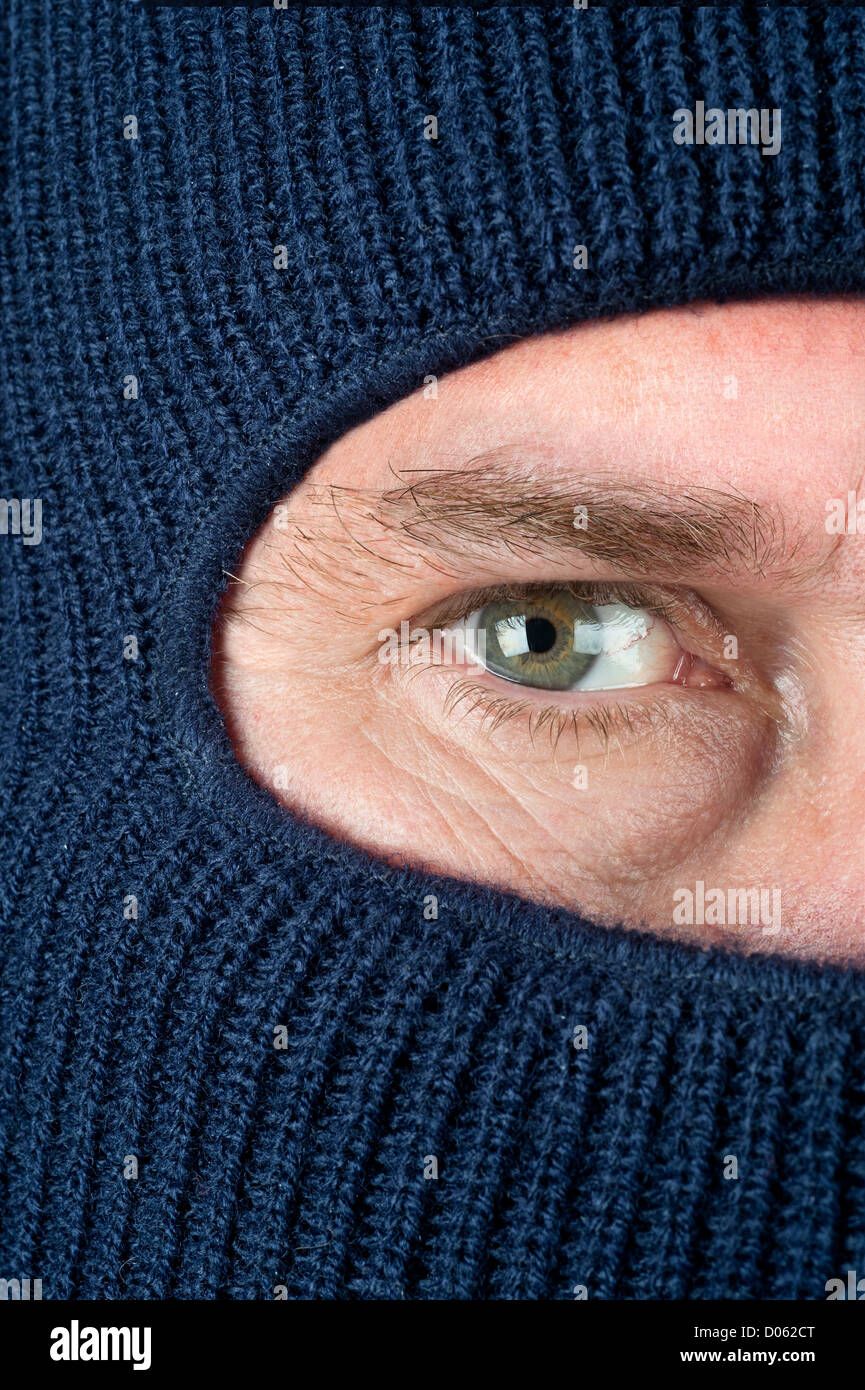 A close up of a burglar peering through a blue ski mask to hide his identity. Stock Photo