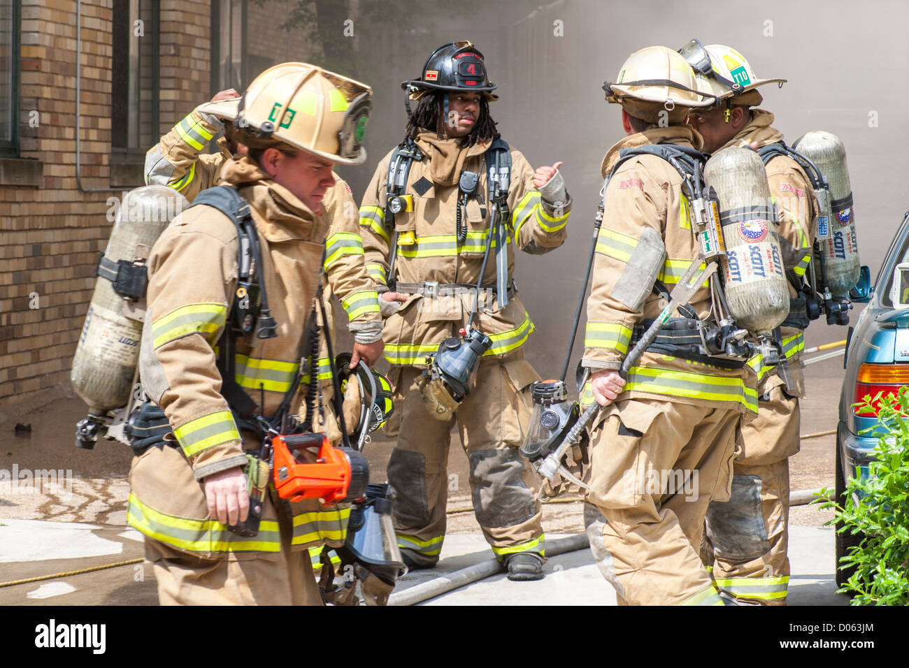 American fire fighters firemen rescue team in front of a burning building, discussing tactics strategy. Diverse crew Caucasian, African-American. Stock Photo