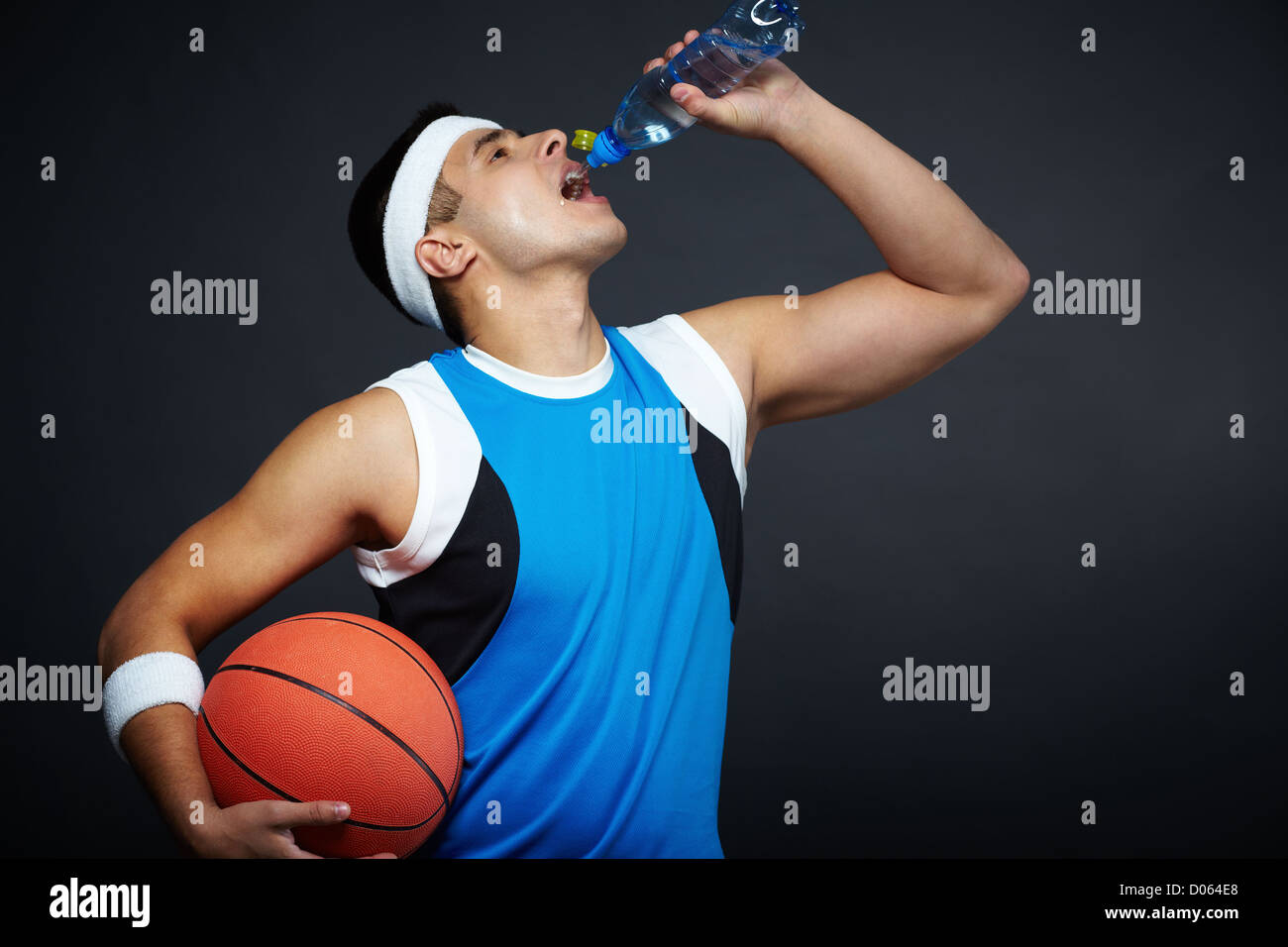 Portrait of handsome guy in sportswear with basket ball drinking water