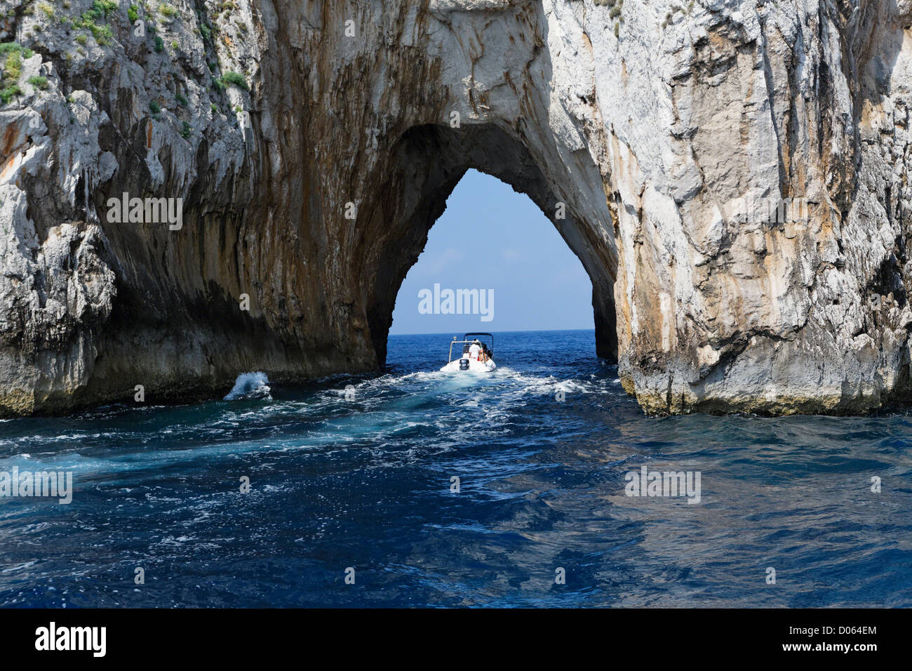 Small Boat is Passing Through a Rock Arch, Faraglioni Rocks, Capri, Campania, Italy Stock Photo