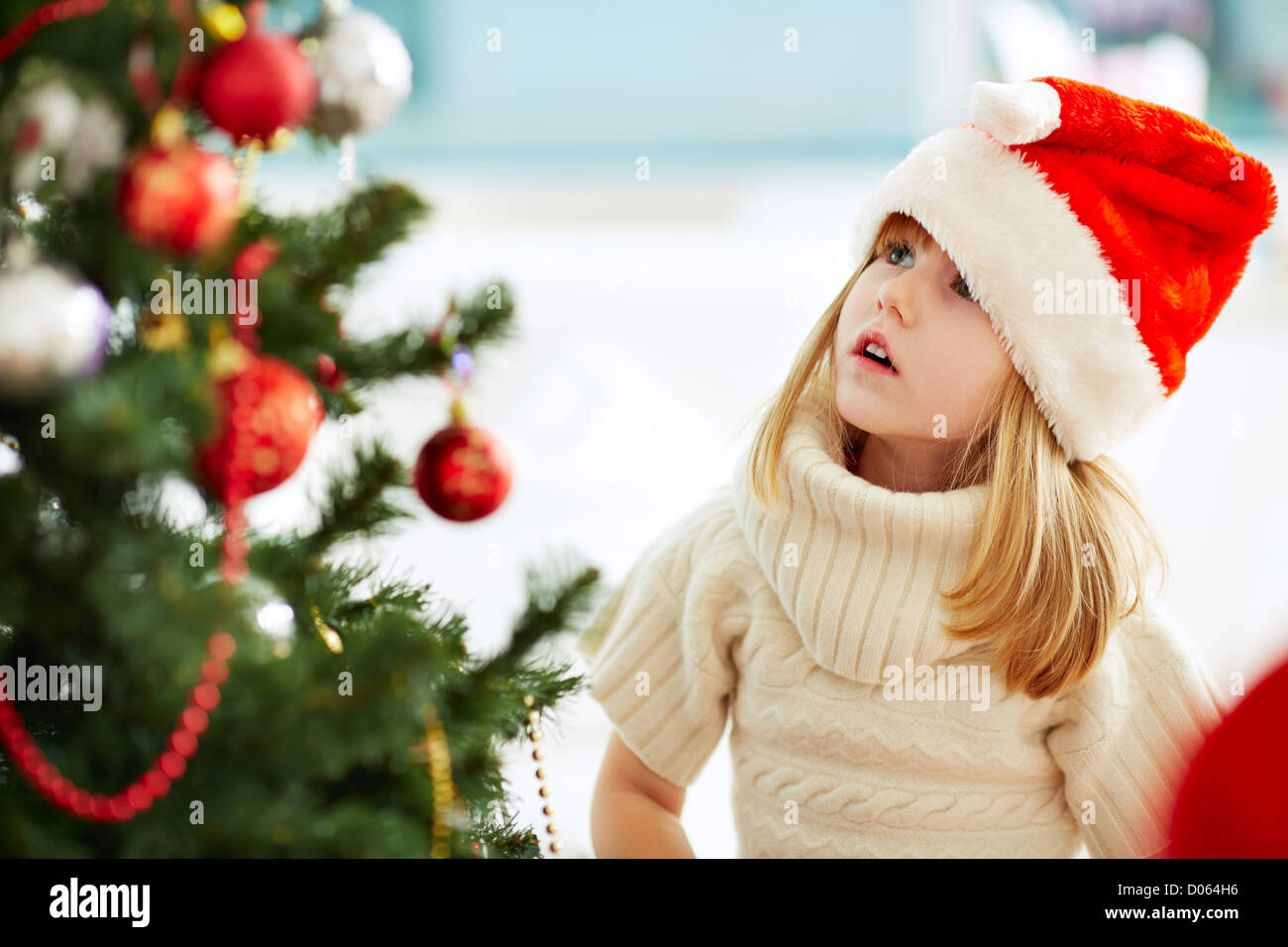 Group of adorable girl in Santa caps looking at xmas tree Stock Photo