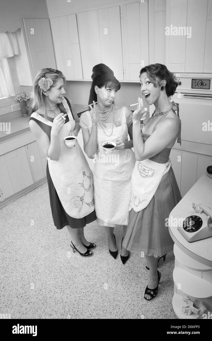Three women gossiping in a kitchen while smoking cigarettes Stock Photo