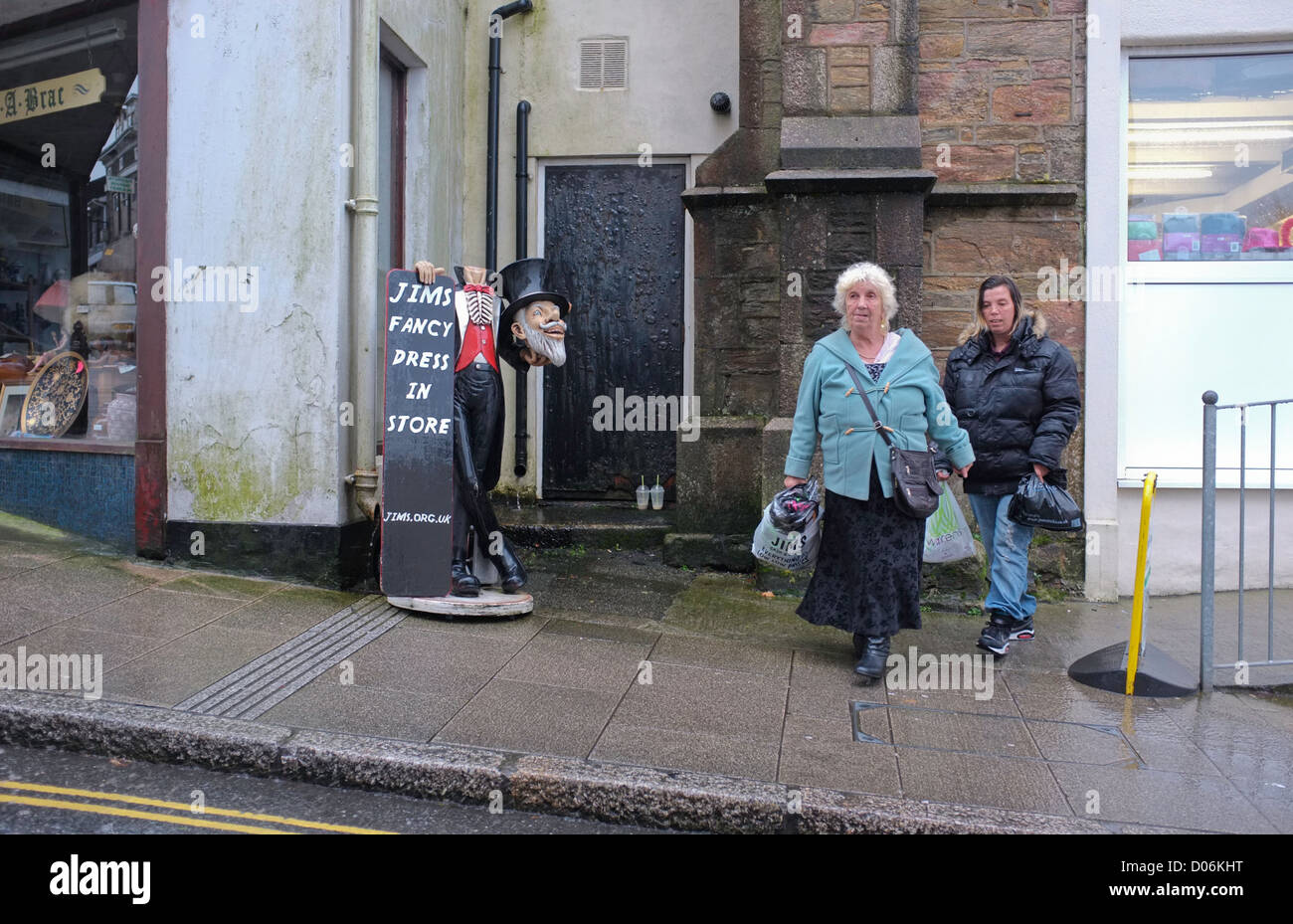 Two women walks past a sign for a fancy dress shop in Redruth, Cornwall Stock Photo