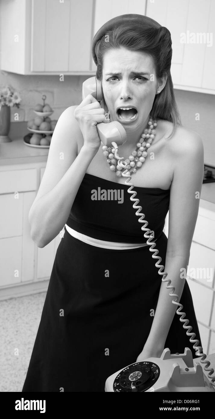 Young Caucasian woman in a kitchen weeps while on the phone Stock Photo