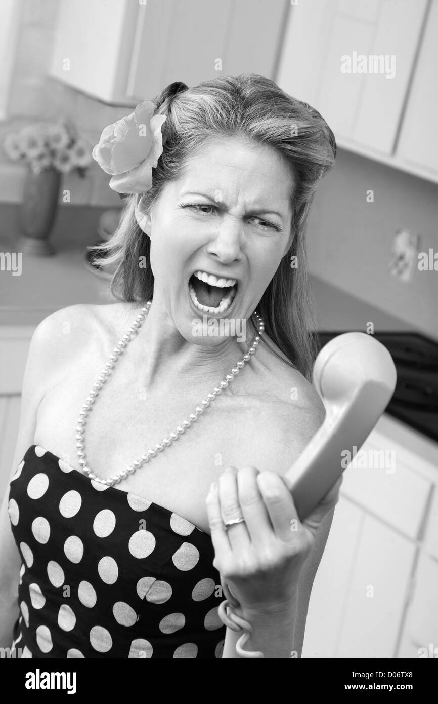 Woman in polka-dot dress yells at phone in kitchen Stock Photo