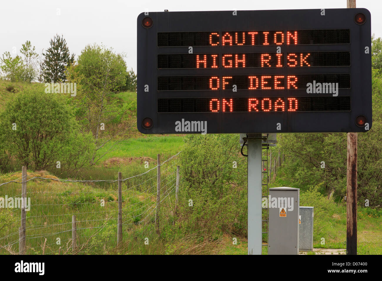 Matrix sign on A85 warning take caution high risk of deer on road with high fence. Crianlarich, Stirlingshire, Scotland, UK Stock Photo