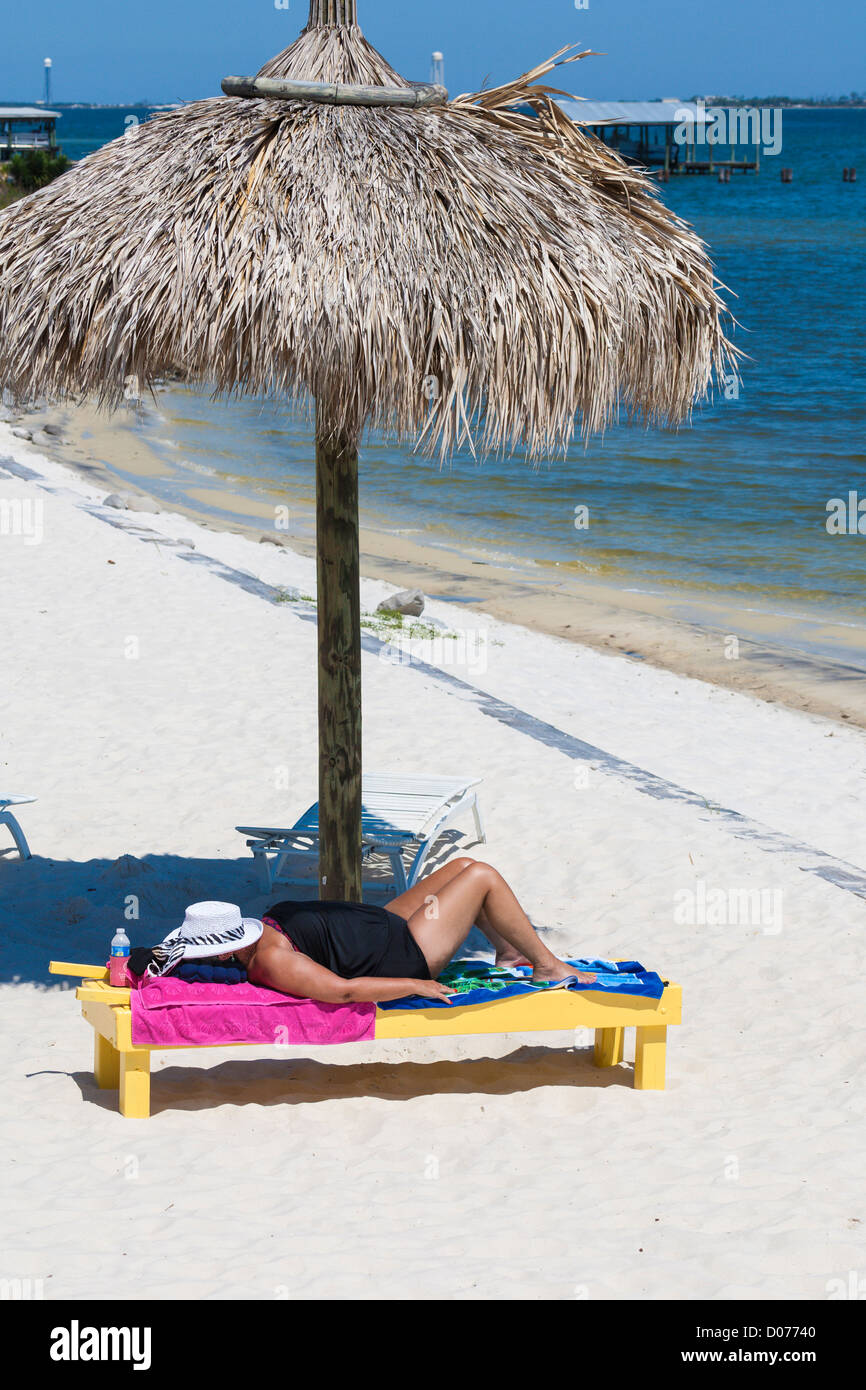 Overweight senior woman lies on lounge chair under umbrella while sunbathing at Navarre, Florida Stock Photo