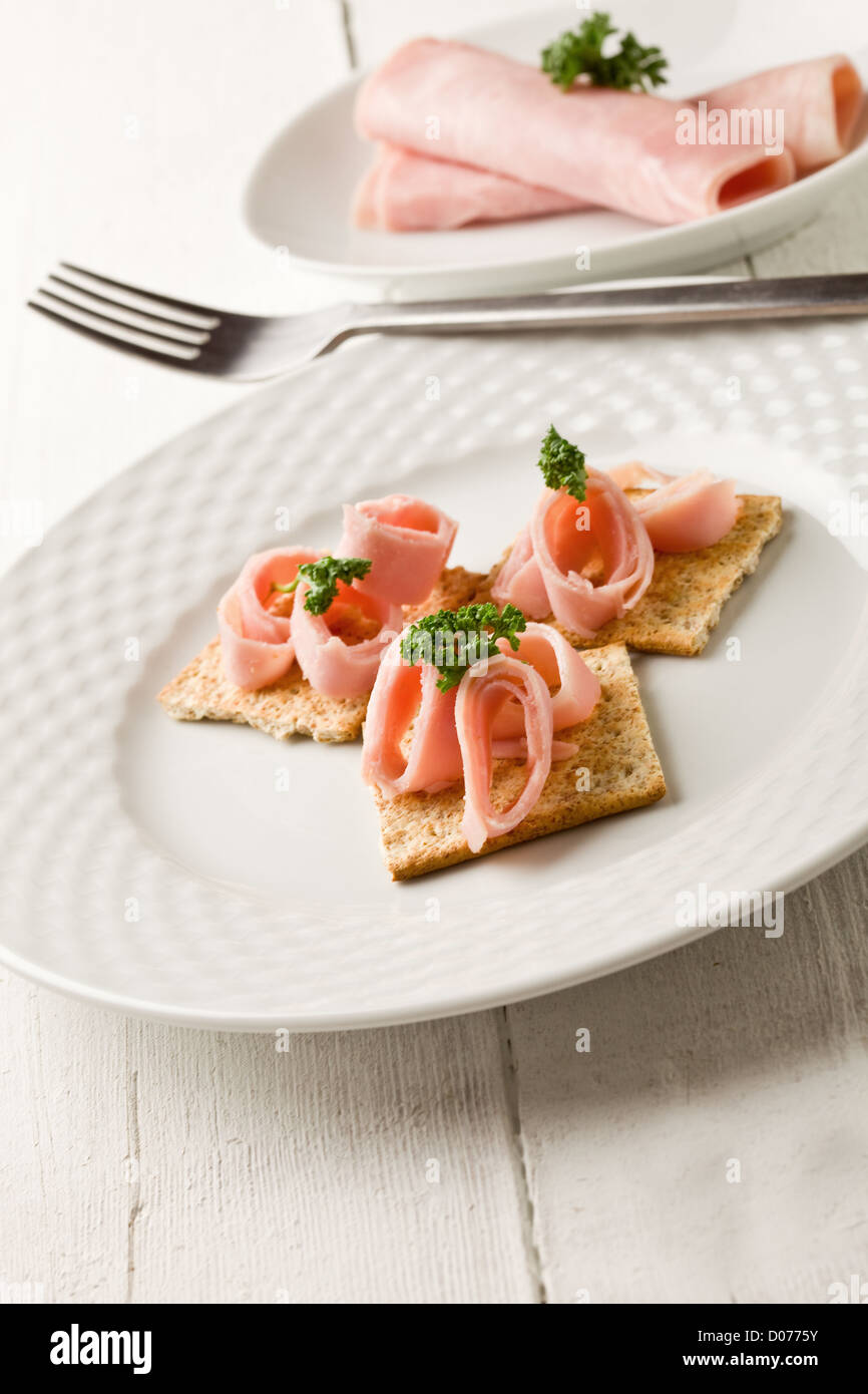 photo of cracker appetizer with ham and parsley on white wooden table